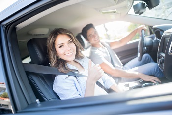 couple sitting in front seat of car smiling at camera, woman holding thumbs up
